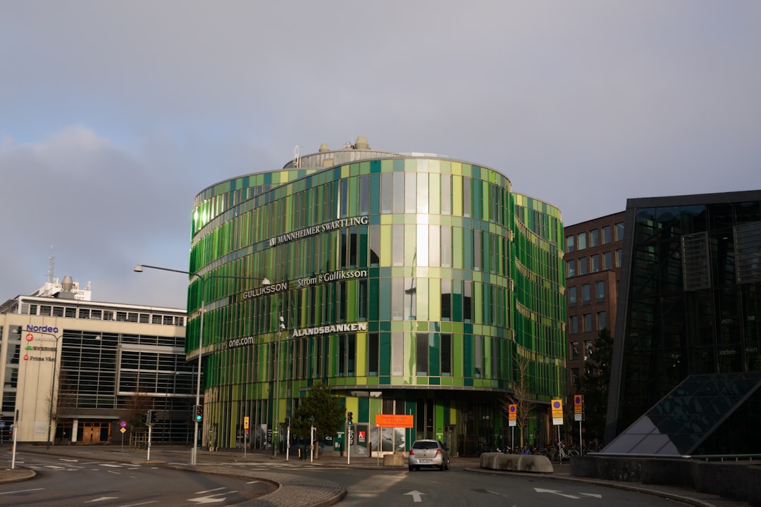 Modern green building with reflective panels under a cloudy sky
